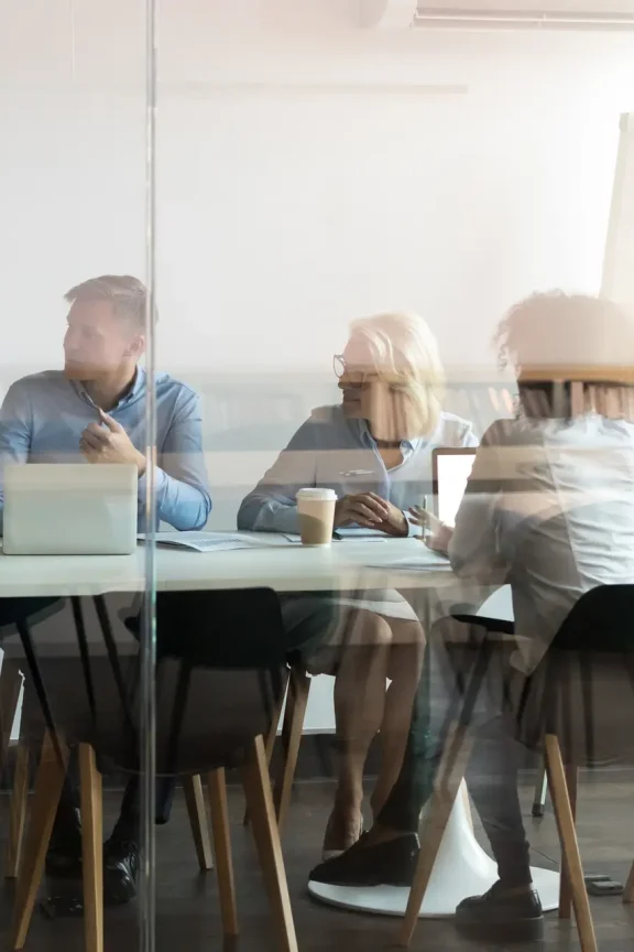 Advertising department brainstorming at modern office boardroom behind closed doors, view through the glass wall. Diverse staff led by ceo discussing new project sharing ideas thoughts and sales pitch